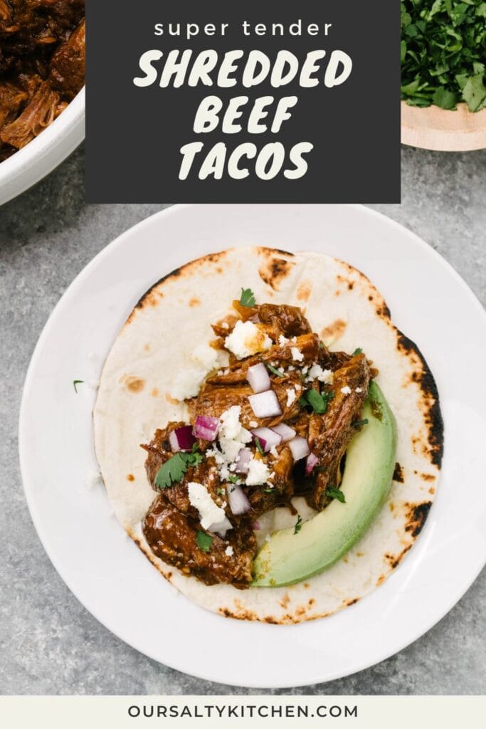A flour tortilla on a white plate piled with Mexican shredded beef, avocado, red onion, queso freso, and cilantro; title bar at the top reads "super tender shredded beef tacos".