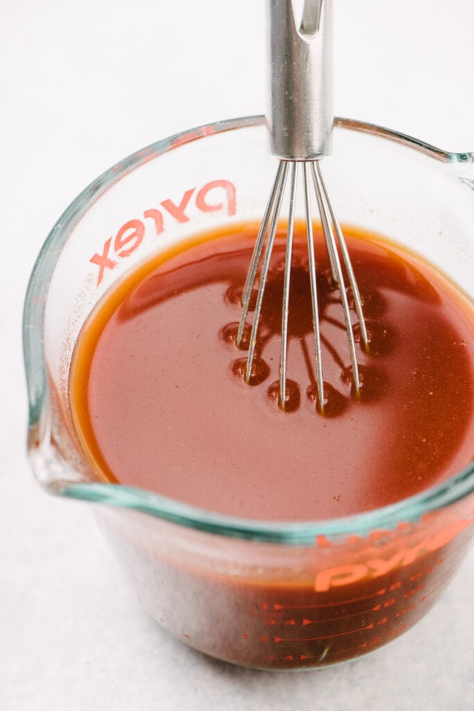 Side view, a whisk in a glass measuring cup filled with beef broth and tomato paste, whisked until smooth.