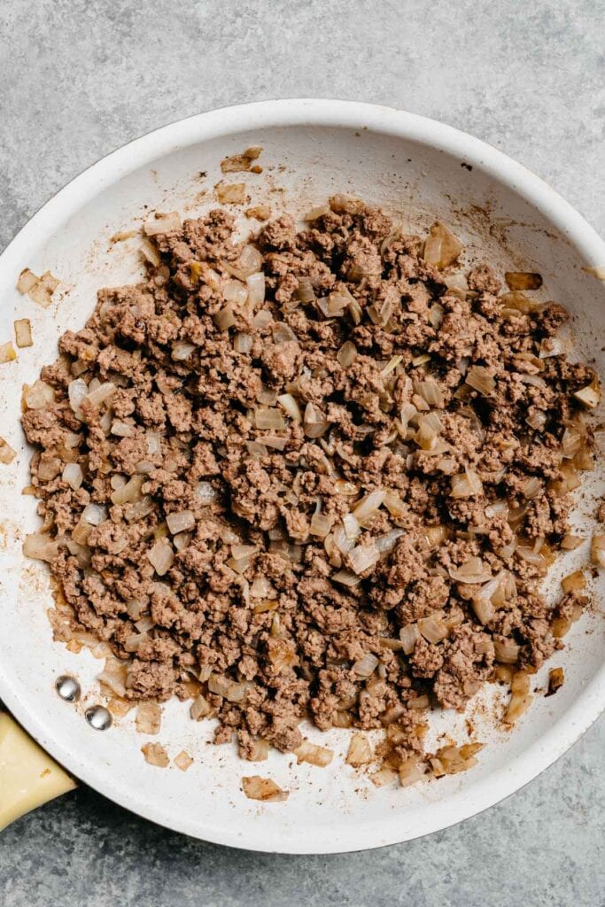Sauteed onions and ground beef in a skillet.
