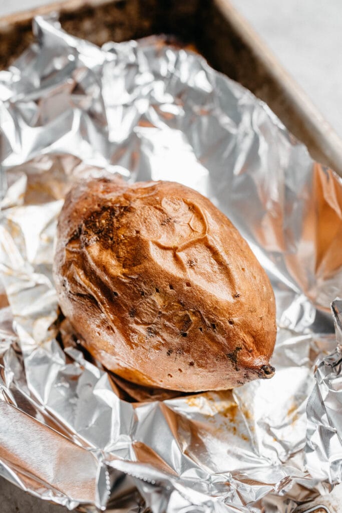 Side view, a roasted sweet potato unwrapped and resting on foil.