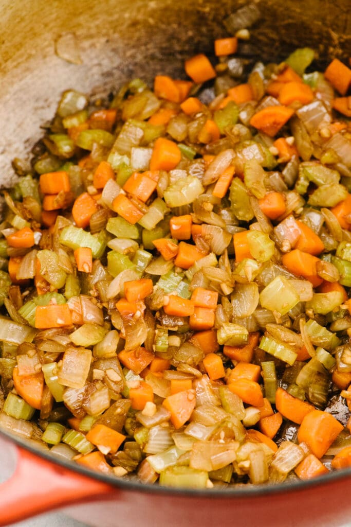 Side view, sauteed onions, carrots, celery, and garlic deglazed with balsamic vinegar in a dutch oven.