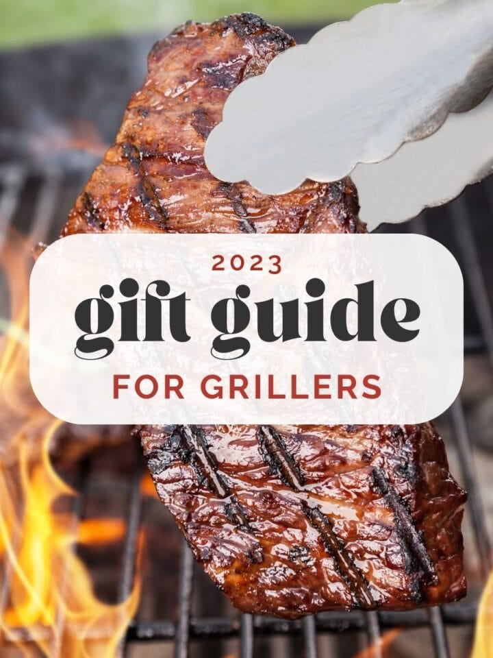 Side view, a steak being lifted from a grill by tongs, surrounded by flames; text overlay reads "2023 gift guide for grillers".