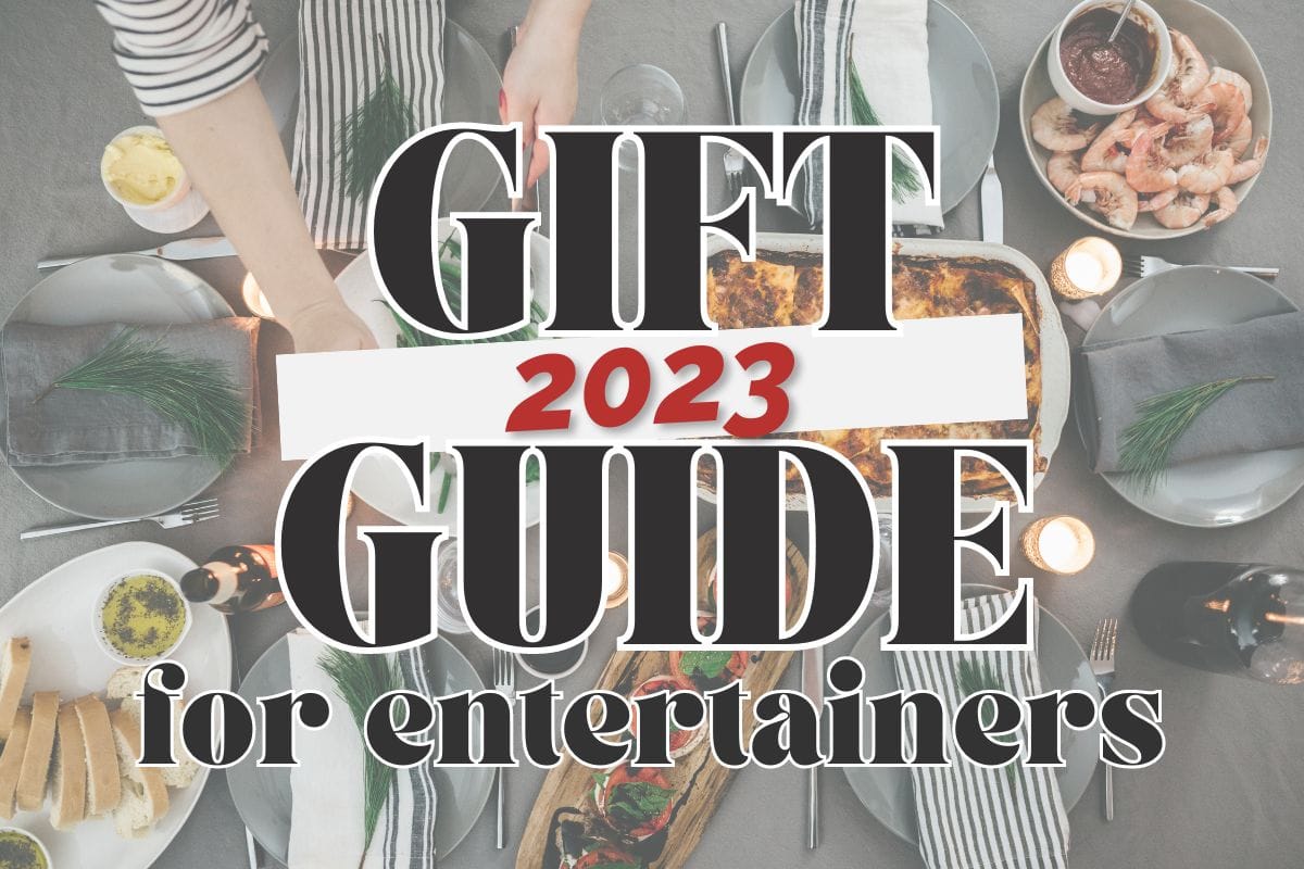 A Christmas table setting with entrees and side dishes, beautiful place settings, and woman's hand serving a side of green beans; text overlay reads "2023 gift guide for entertainers".