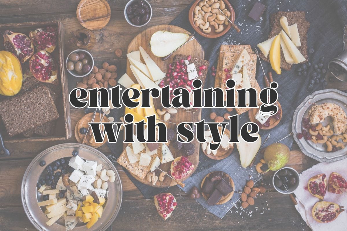 Overhead view of various cheese plates, nuts, fruits, and olives on trays and wood boards; text overlay reads "entertaining with style".