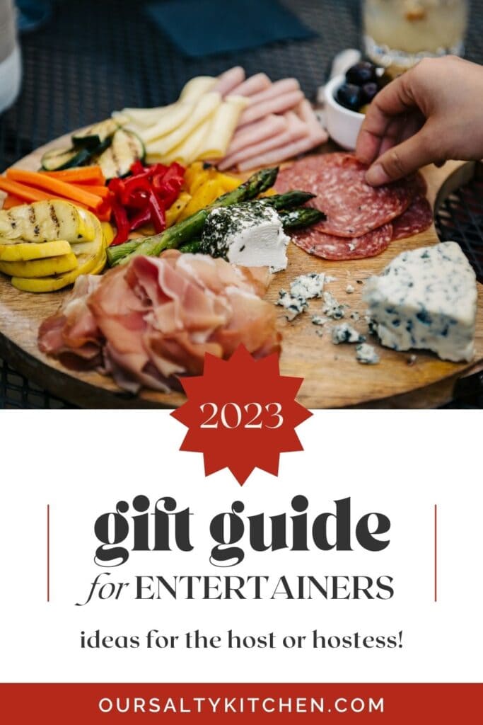 Side view, a host holding a beautiful charcuterie board, with a guest taking a pice of salami; text box below reads "2023 gift guide for entertainers".