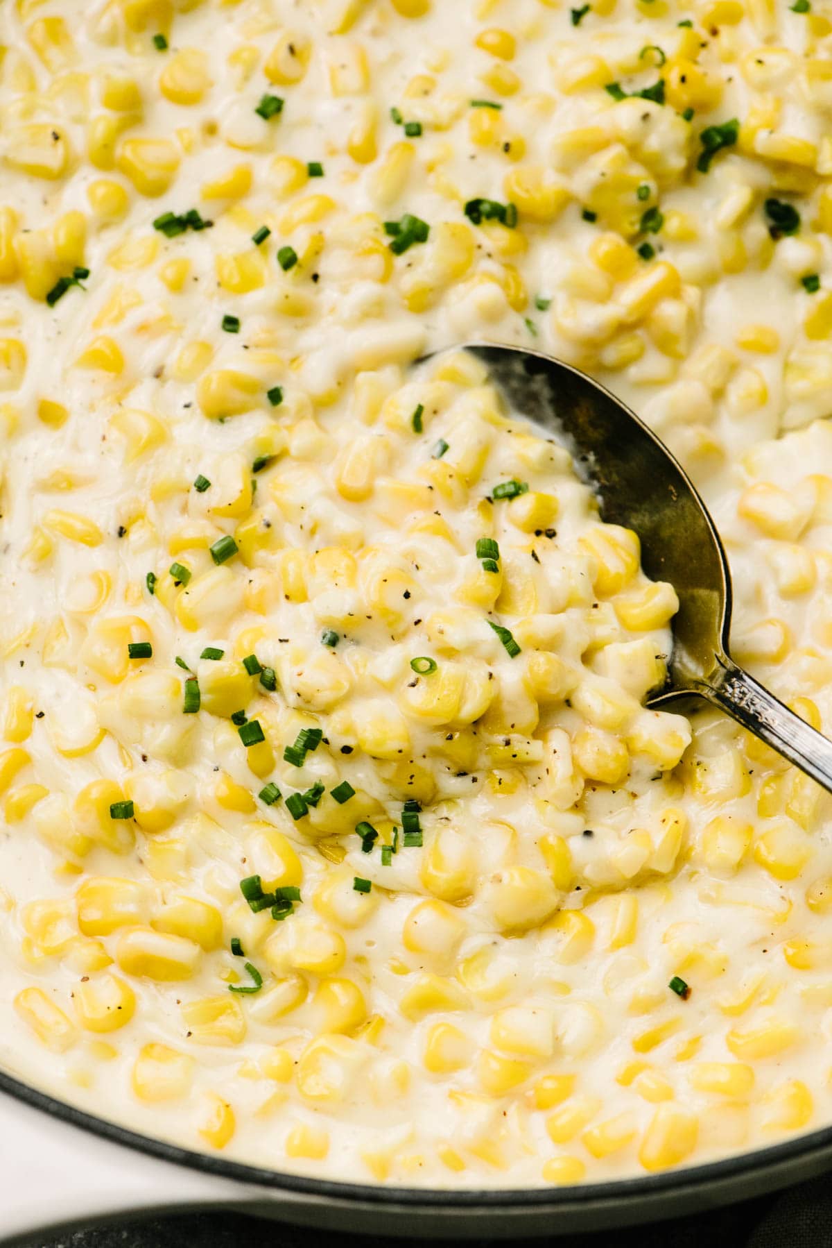 Side view, a serving spoon tucked into a skillet of homemade creamed corn.