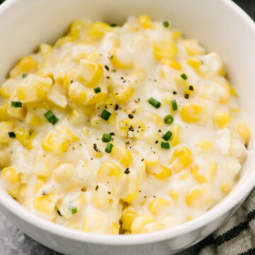 Side view, creamed corn in a small white bowl garnished with fresh chives and ground pepper.
