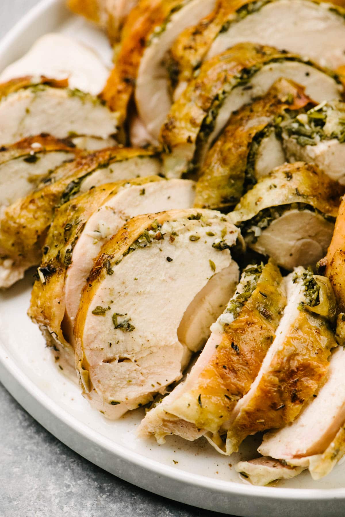 Side view, carved pieces of herb roasted chicken breast on a white plate.
