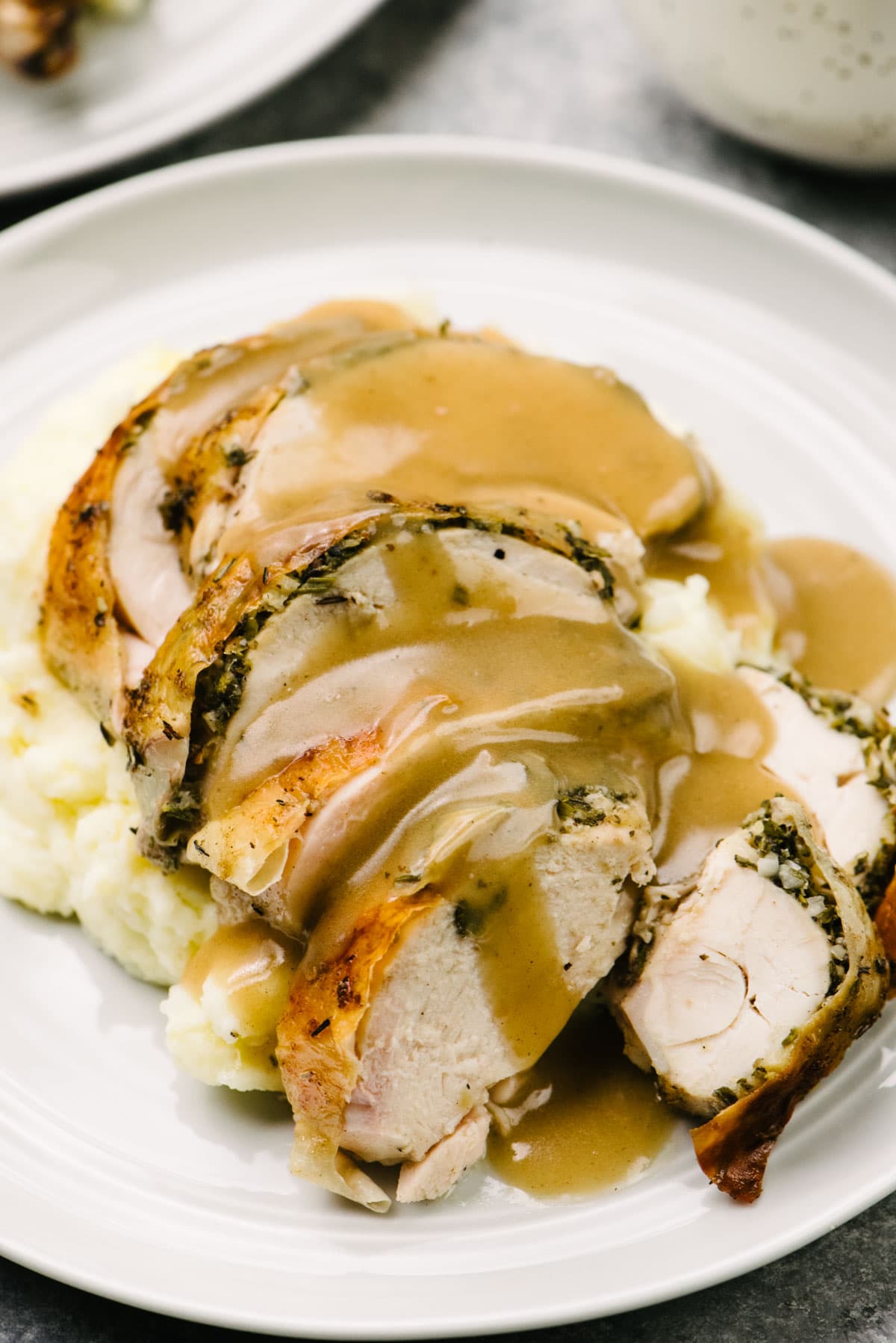 Side view, herb roasted chicken breast pieces over mashed potatoes, smothered with gravy, on a white plate.