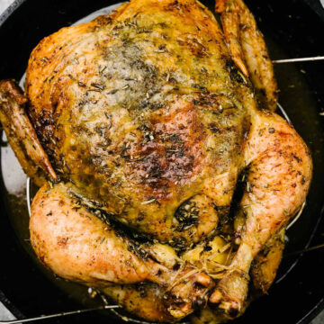 An herb roasted chicken fresh from the oven with golden brown skin in a cast iron skillet.