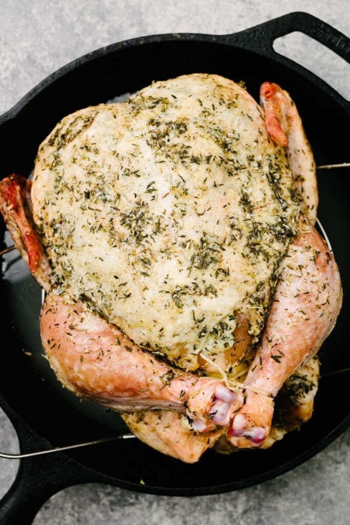 A trussed whole chicken covered with herbs on a trivet in a cast iron skillet.