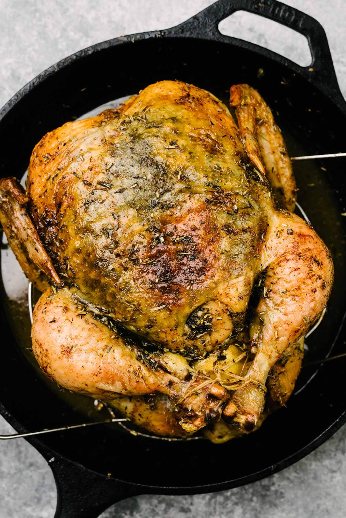 An herb roasted chicken with crispy, golden brown skin on a trivet nested into a cast iron skillet.