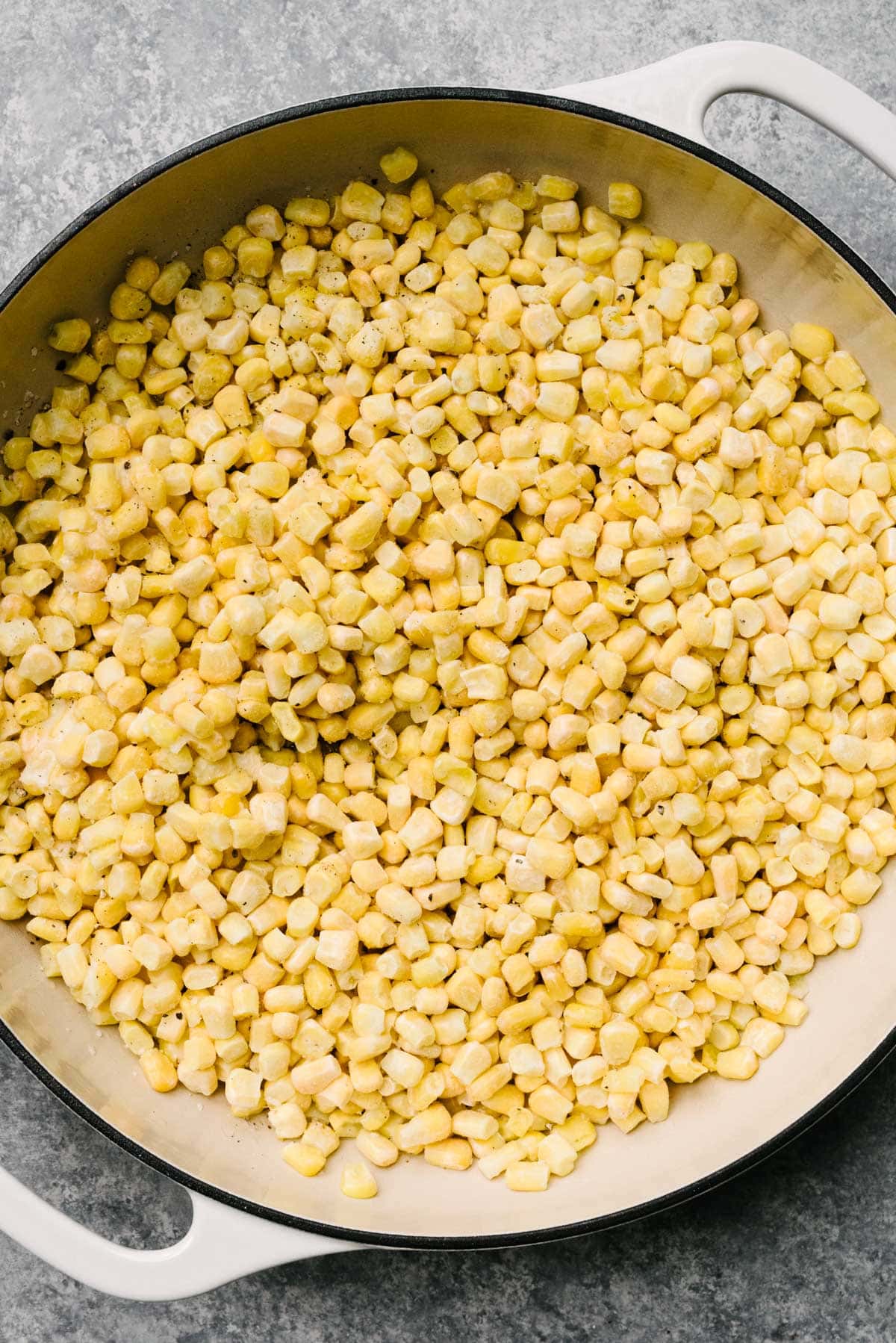 Frozen corn tossed with melted butter in a large grey enameled skillet.