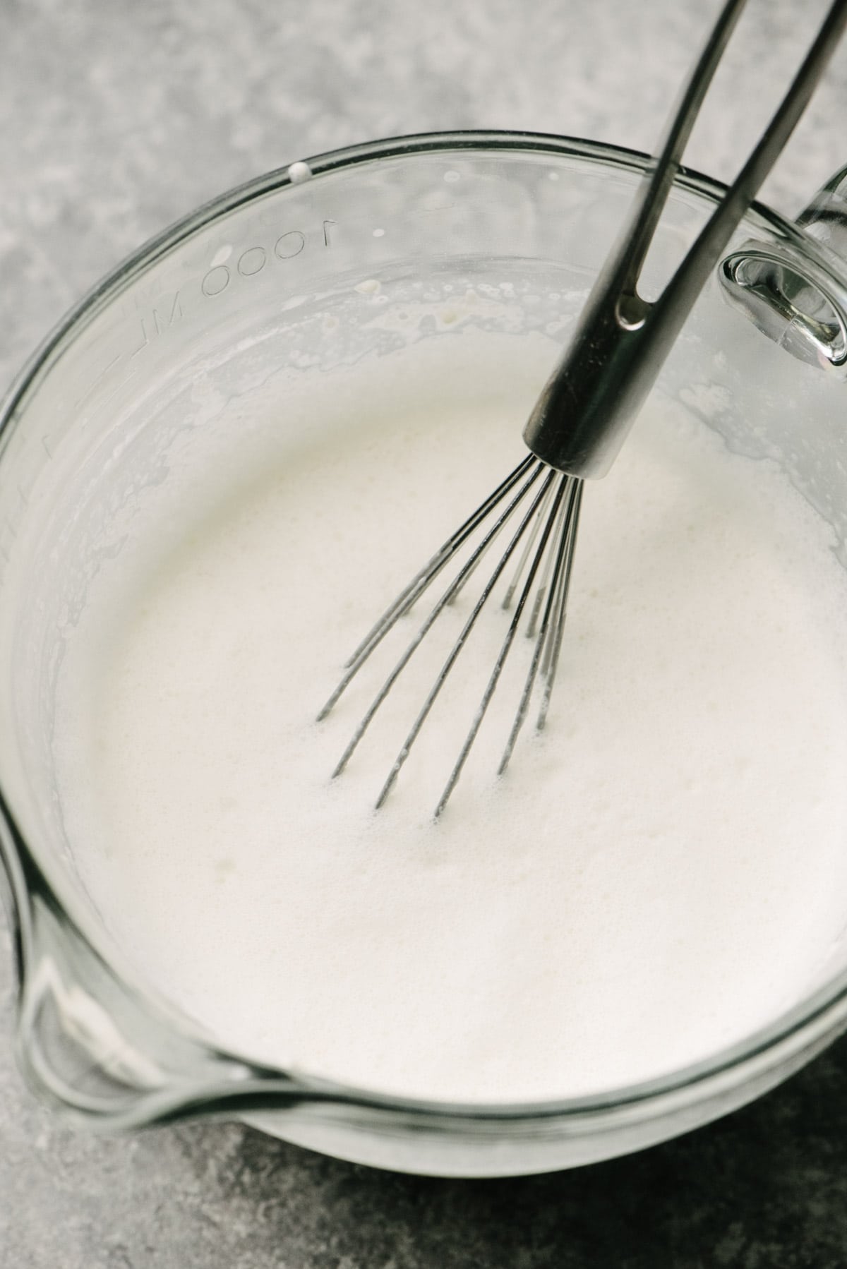 Side view, milk, heavy cream, and flour whisked until foamy in a large glass measuring cup.