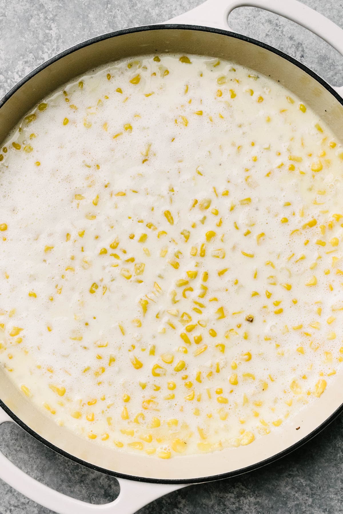 Corn kernels mixed with heavy cream, milk, flour, and sugar in a large grey enameled skillet.