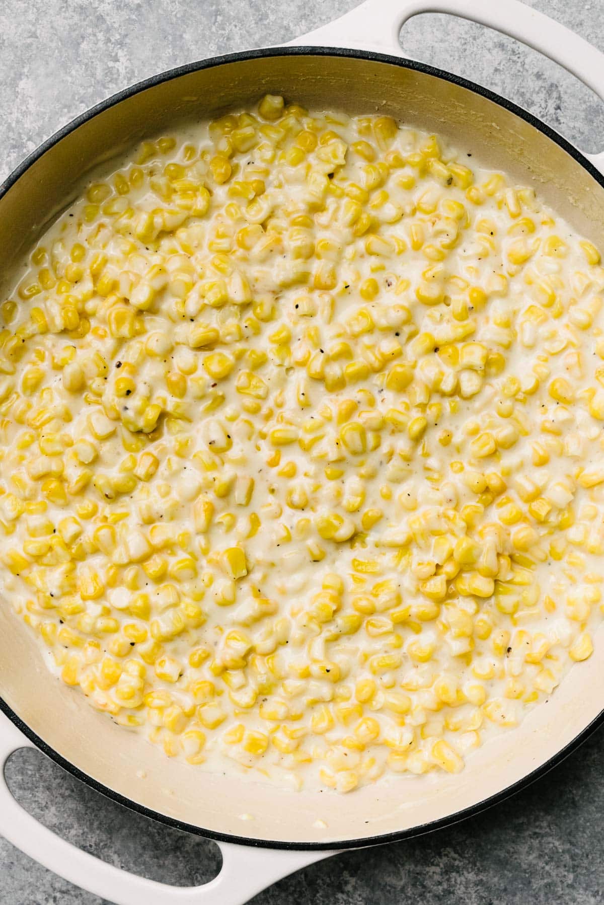 Frozen corn kernels cooked down in a thick cream sauce in a large grey skillet.