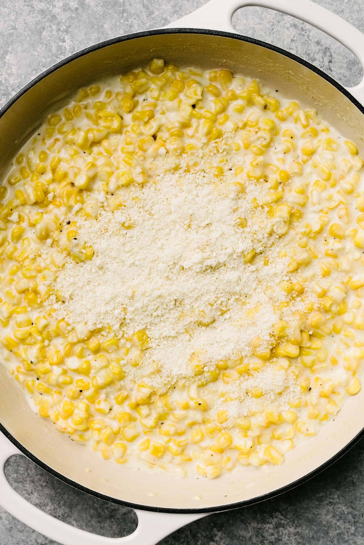 Grated parmesan cheese sprinkled over homemade cream style corn in a large grey skillet.
