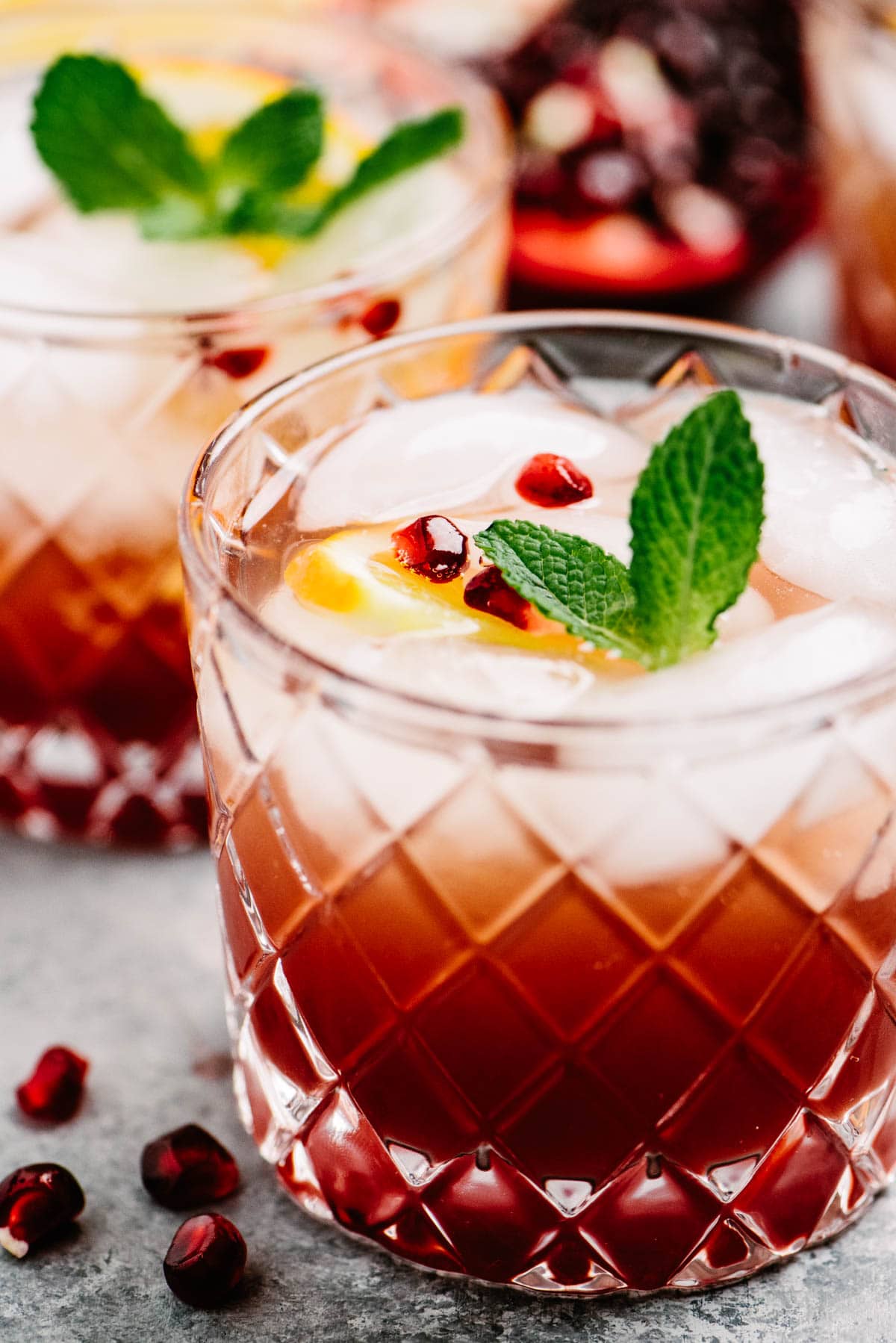 Side view, two prosecco punch cocktails with pomegranate on a concrete background, garnished with pomegranate seeds, orange slices, and a mint sprig.