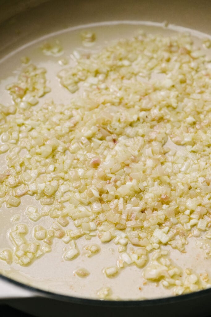 Side view, finely chopped shallots and onions sautéing in a large skillet.