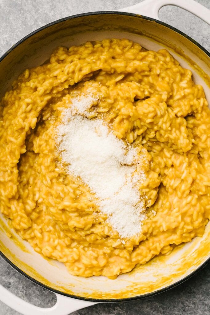 Finely grated parmesan cheese added to pumpkin risotto in a light grey skillet.