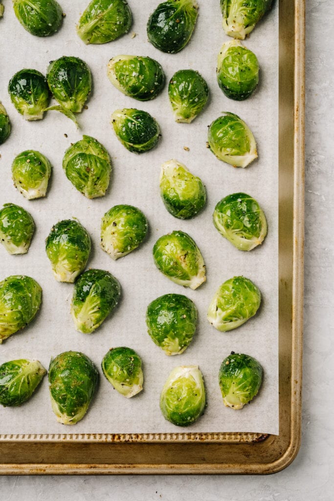 Halved Brussels sprouts coated with oil and seasonings arranged cut side down on a parchment lined baking sheet.