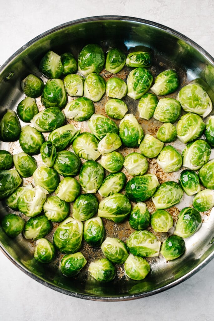 Halved Brussels sprouts cut side down in a skillet, sautéing in bacon fat.
