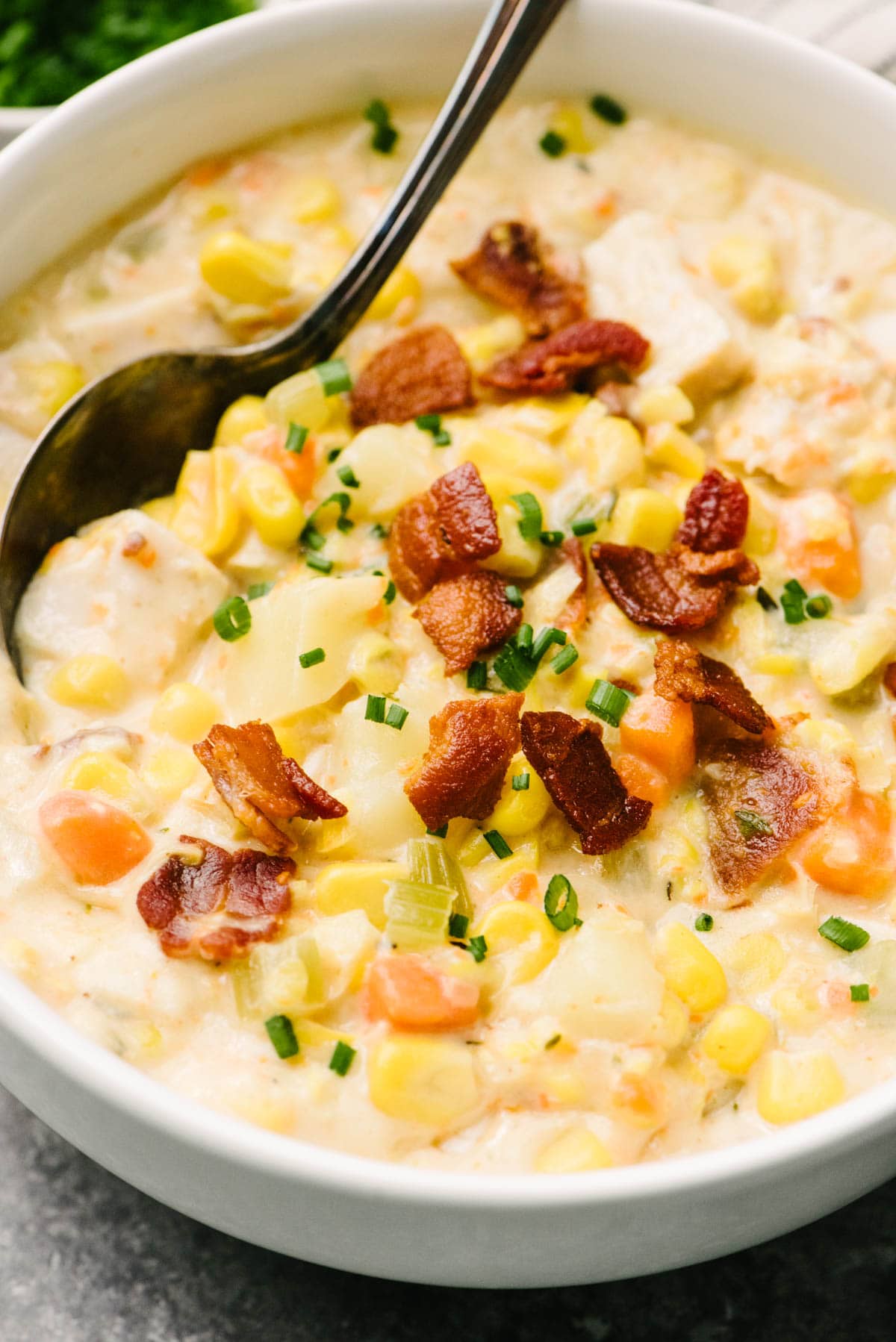 Side view, a spoon tucked into a bowl of creamy turkey corn chowder, garnished with chopped bacon and fresh chives.
