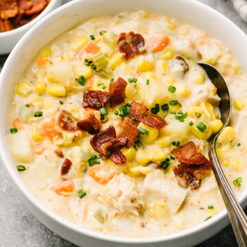 Side view, a spoon tucked into a bowl of turkey corn chowder garnished with cooked bacon and fresh chives.