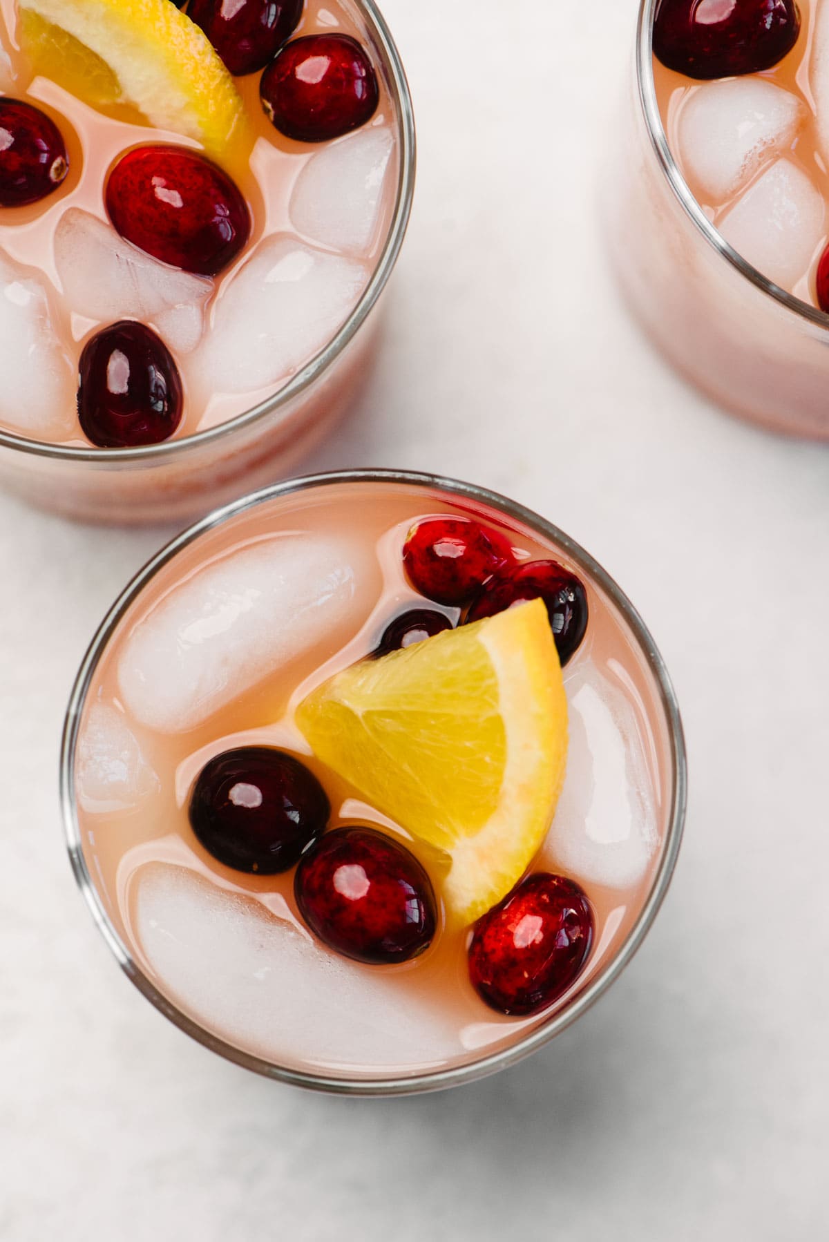 From overhead, several glasses of whiskey punch  on a concrete background, garnished with orange slices and fresh cranberries.