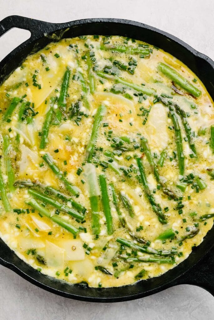 A partially baked asparagus frittata in a cast iron skillet - with firm edges but a soft center - ready to finish baking in the oven.
