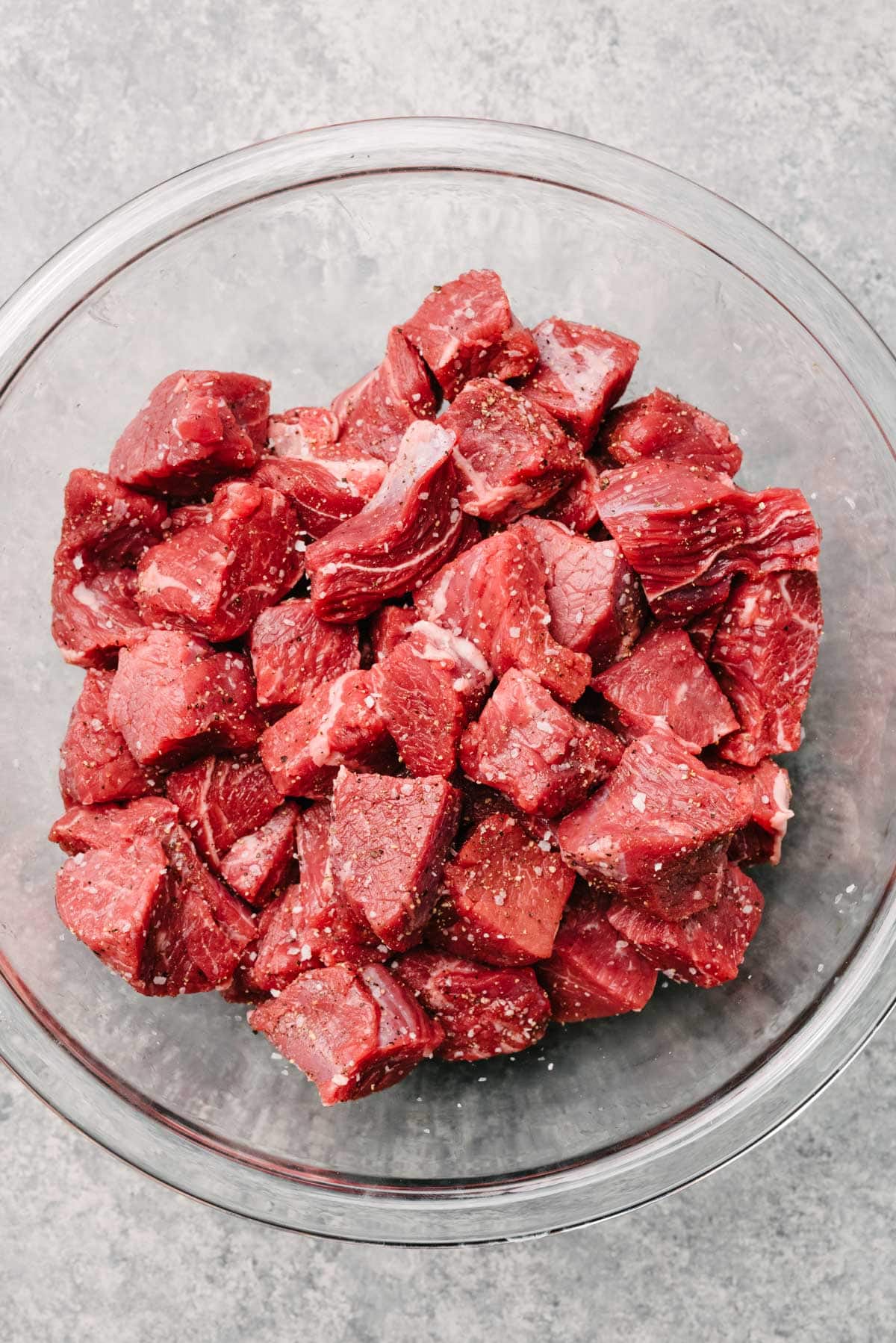 Raw stew meat seasoned with salt and pepper in a large mixing bowl.