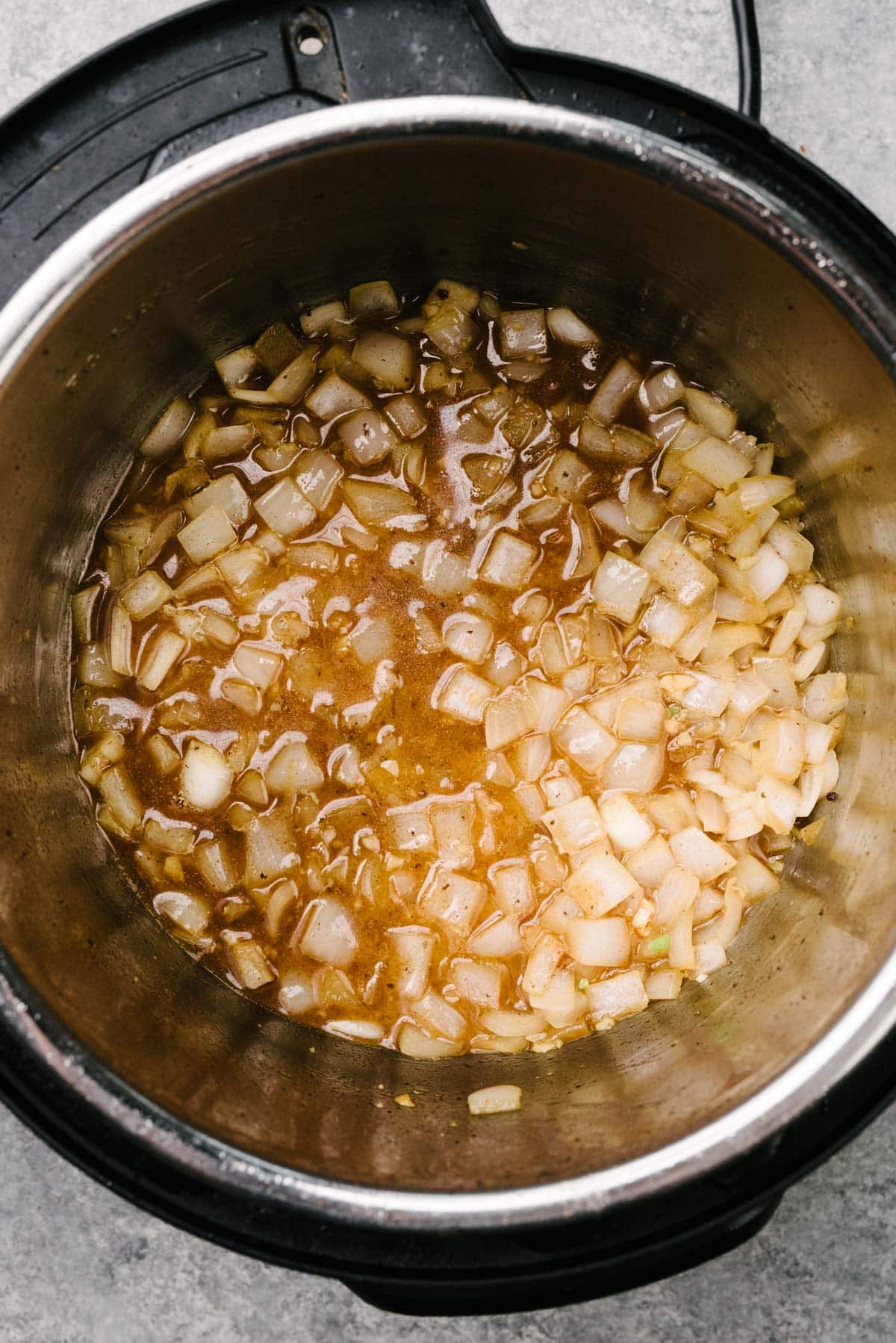 Wine added to sautéed onions and garlic in an Instant Pot to deglaze the surface and prepare for pressure cooking.