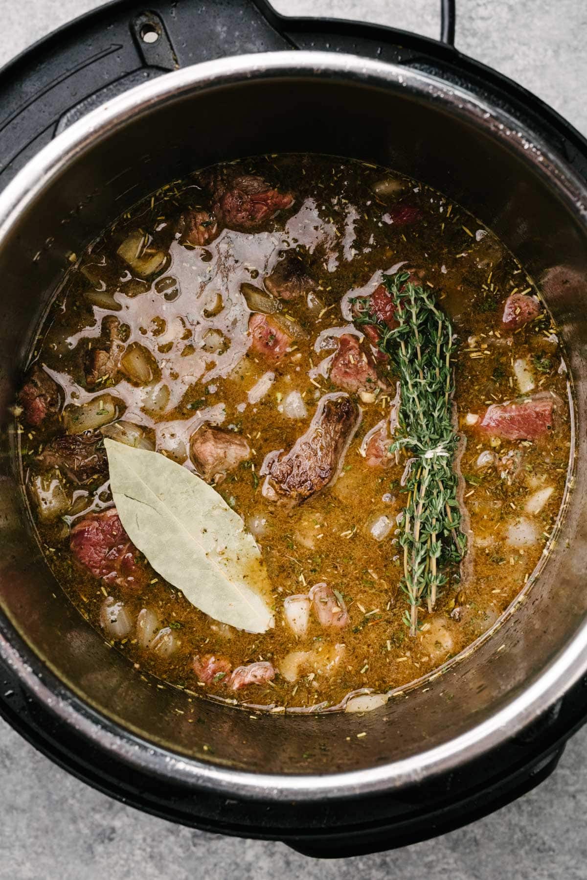 Seared chunks of stew meat, sautéed onions and garlic, wine, beef broth, Worcestershire sauce, fresh thyme, and a bay leaf in an Instant Pot before pressure cooking.