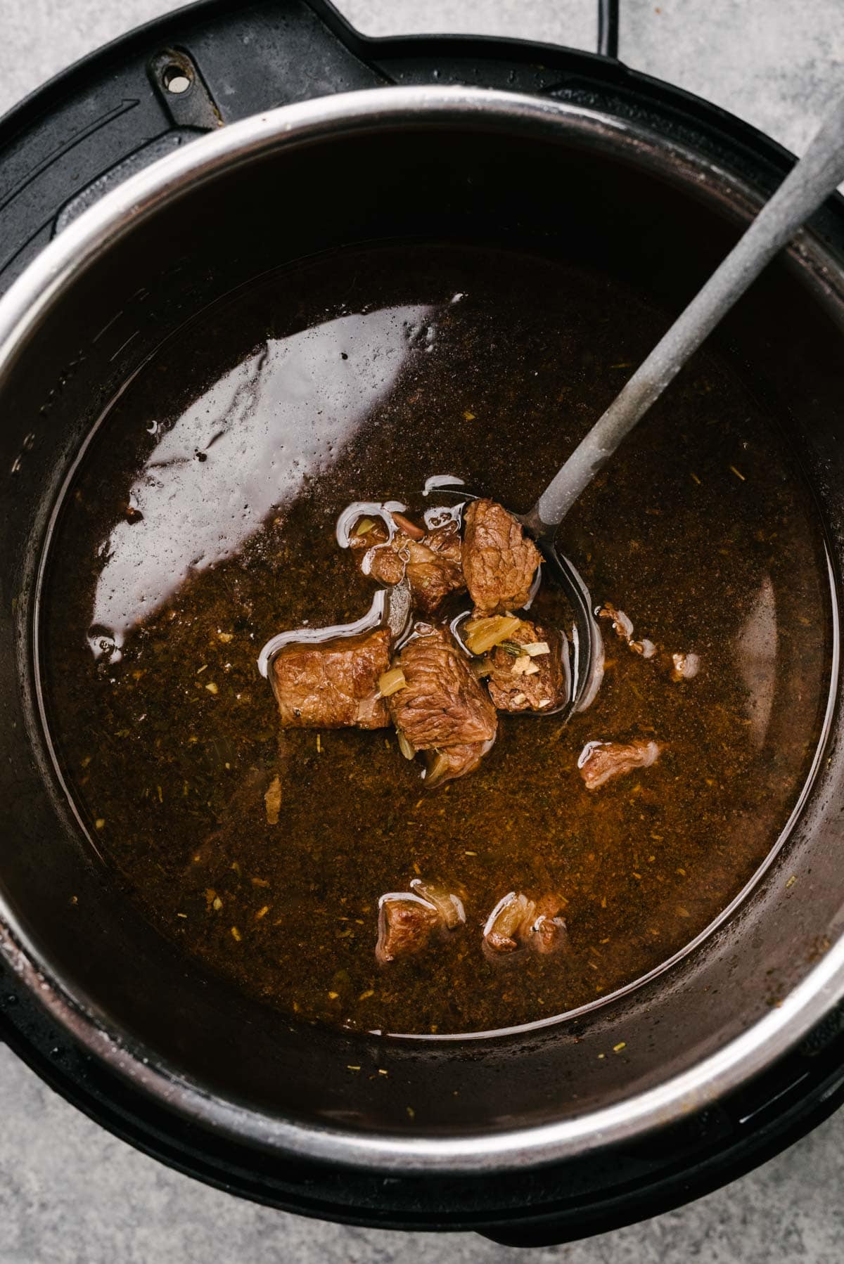 A ladle tucked into an Instant Pot showing tender beef tips in gravy, before thickening the gravy.