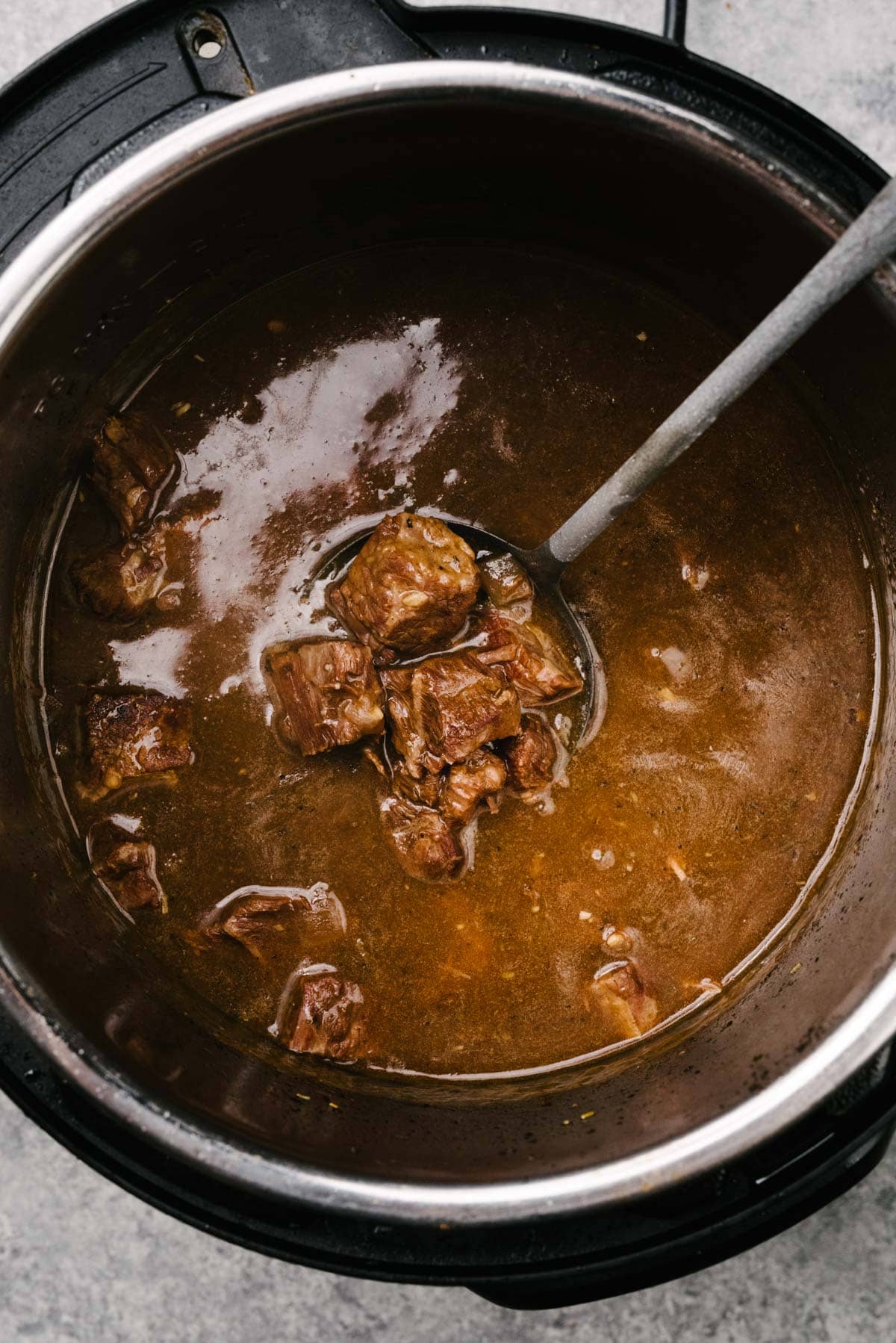 A ladle tucked into an Instant Pot showing tender pieces of beef tips swimming in a rich, thick gravy.