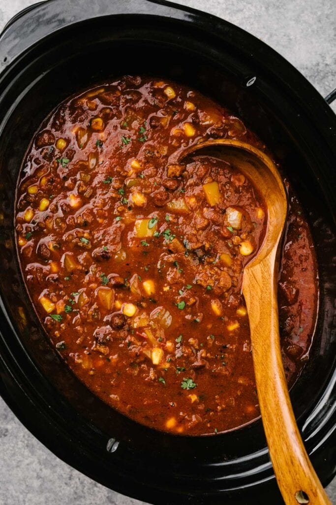A wood ladle tucked into taco soup seasoned with lime juice and fresh cilantro in a slow cooker.