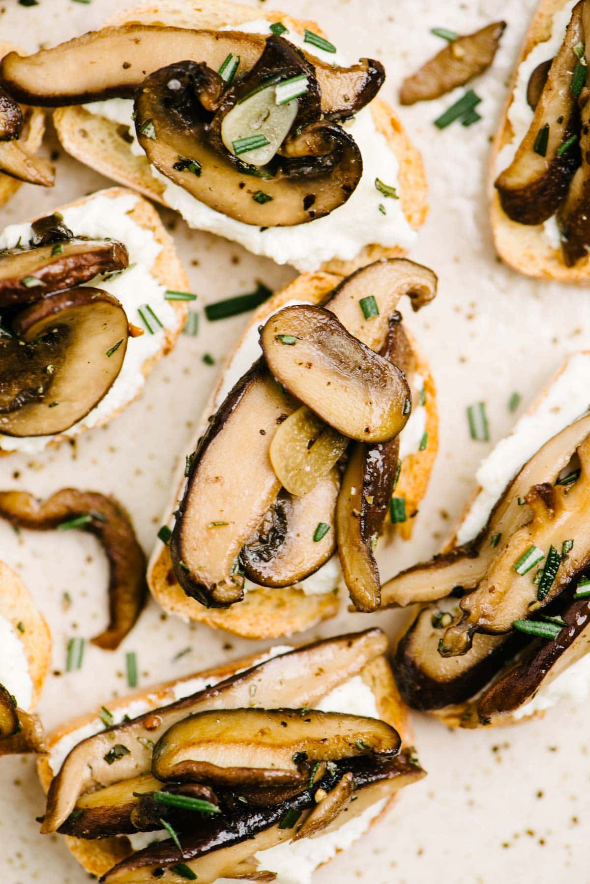 Several pieces of crostini topped with ricotta cheese and sautéed mushrooms on a speckled tan platter.