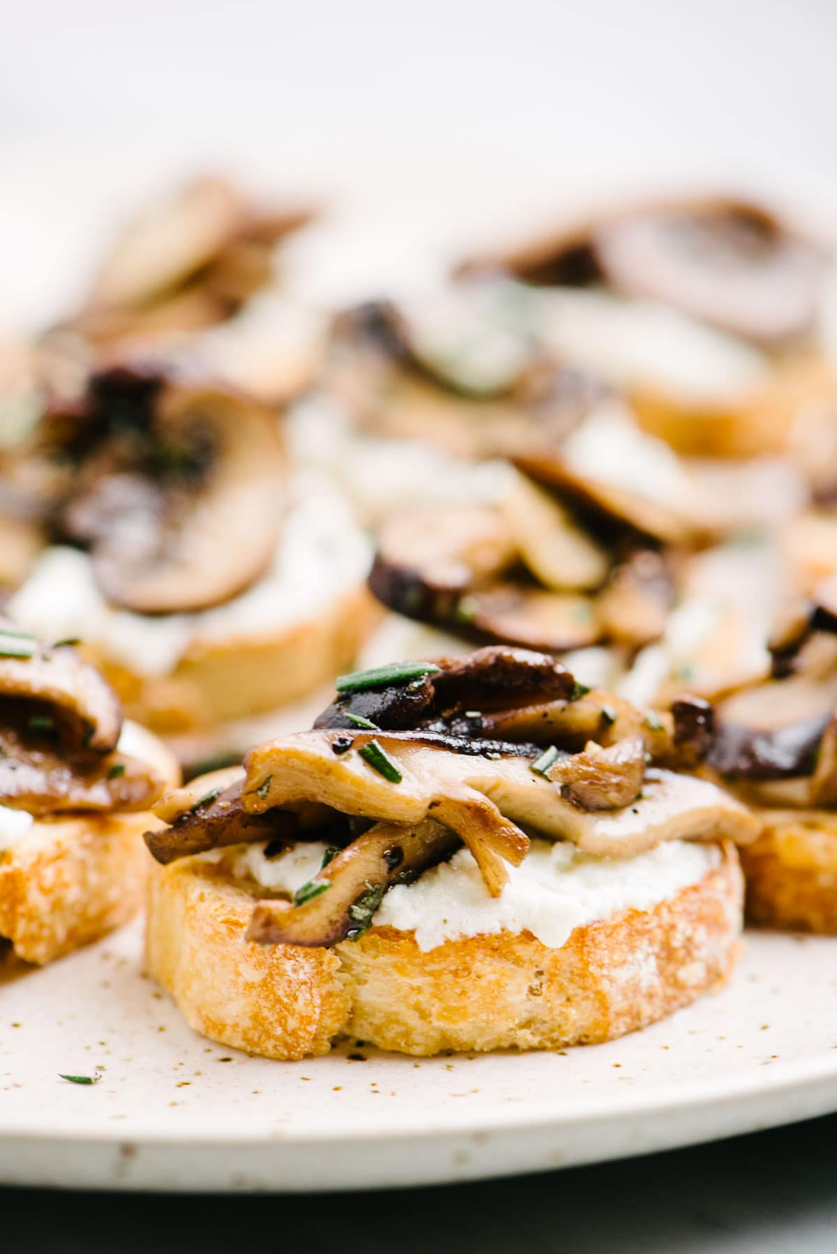 Side view, mushroom crostini on a platter garnished with fresh chopped rosemary.