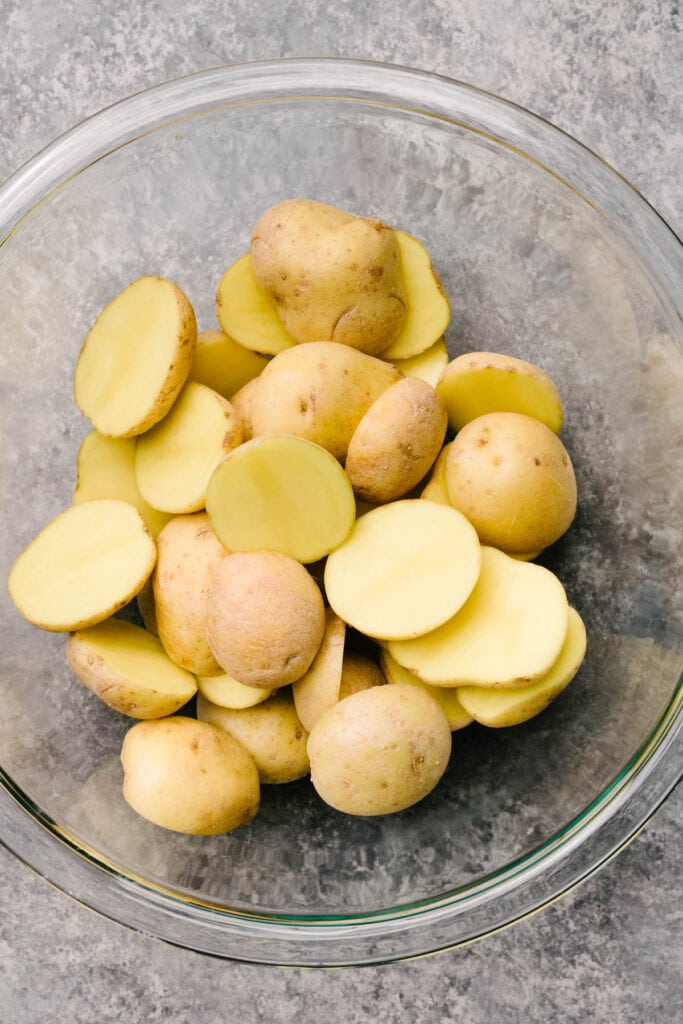 Baby yukon gold potatoes sliced in half and placed into a glass mixing bowl.