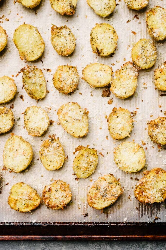 Parmesan crusted potatoes halfway through baking - the potatoes are flipped over on a baking sheet with additional parmesan cheese sprinkled on top.