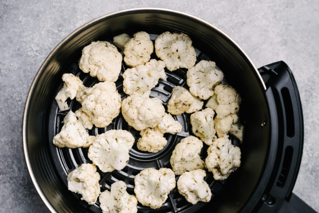 Cauliflower florets tossed with olive oil, salt, and pepper arranged in an even layer in an air fryer basket.