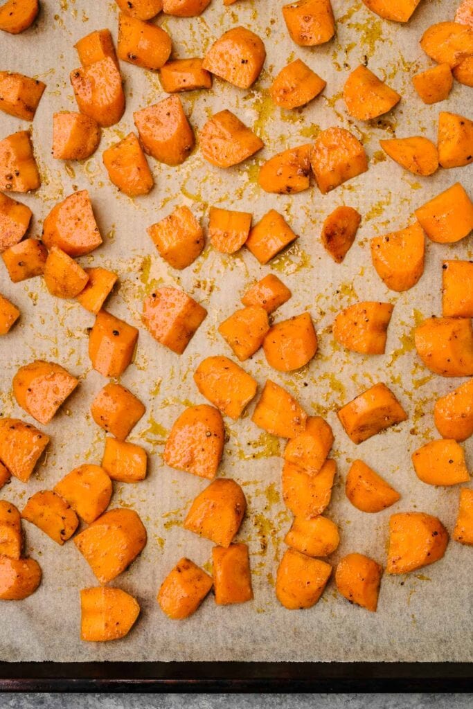 Sliced carrots tossed with olive oil and seasonings on a parchment lined baking sheet.