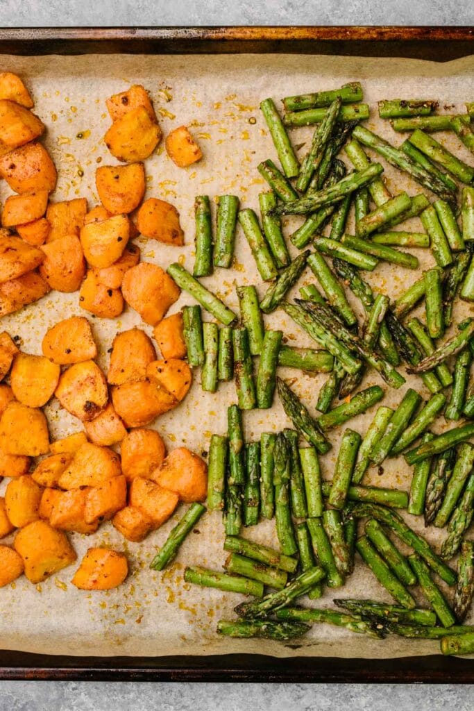Roasted carrots and asparagus on a parchment lined baking sheet.