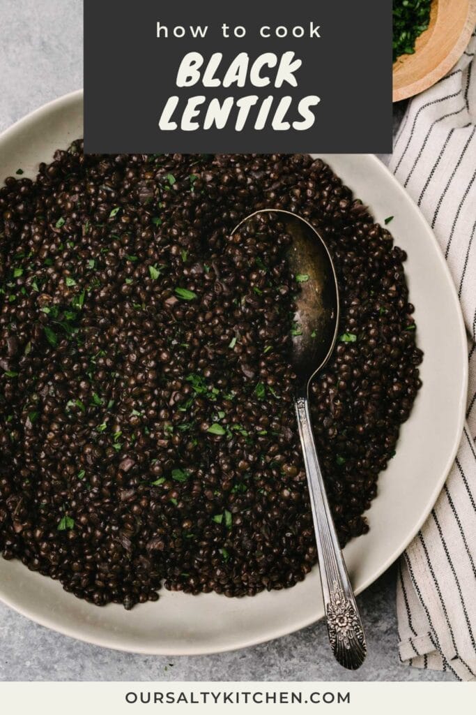 A silver serving spoon tucked cooked black lentils in a shallow serving bowl, garnished with fresh parsley; a striped linen napkin is tucked to the side; title bar at the top reads "how to cook black lentils".