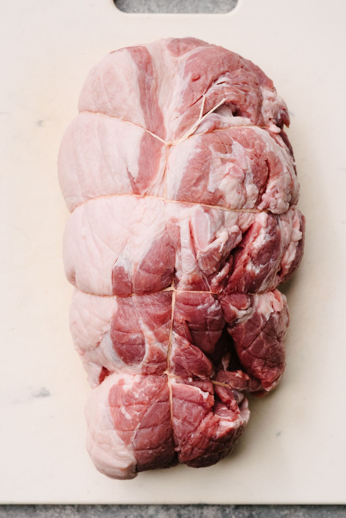A boneless Boston butt trussed with kitchen twine on a white cutting board.