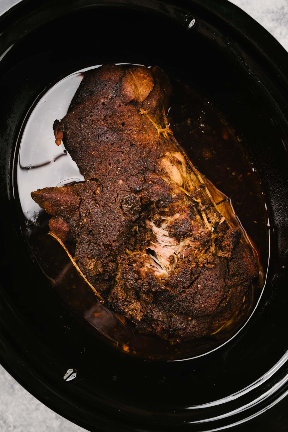 A cooked Boston butt pork roast in a crockpot with a portion of the pork "pulled" to show it has been cooked through.