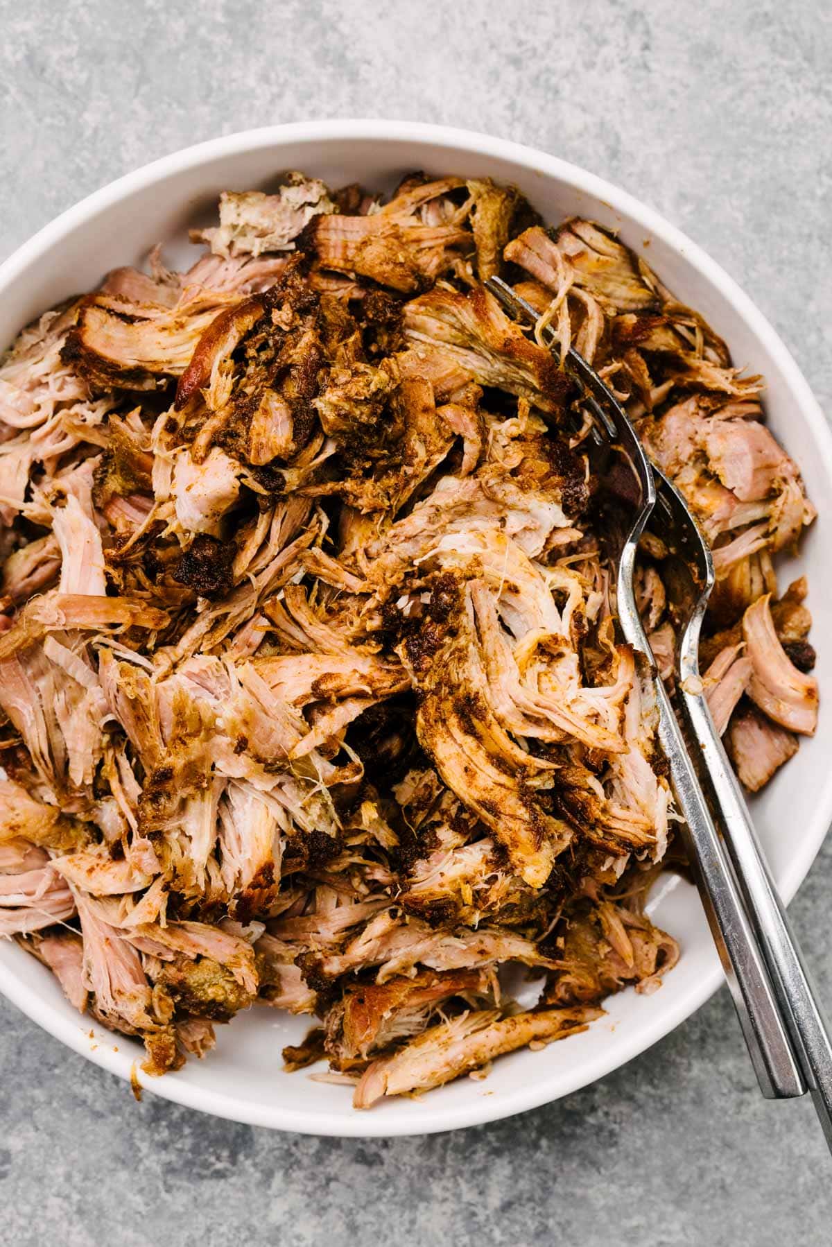 Shredded pulled pork in a large white bowl with two forks.