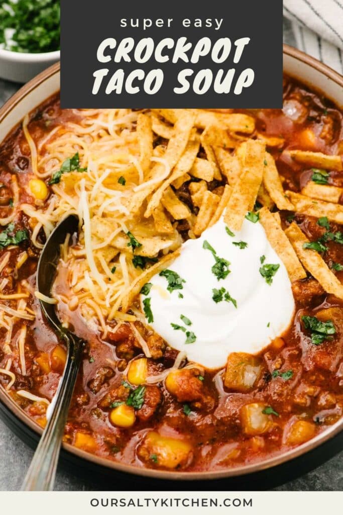 A soup spoon tucked into a bowl of crockpot taco soup, garnished with sour cream, shredded cheese, tortilla strips, and chopped cilantro; a small bowl of chopped cilantro and a striped linen napkin are in the background; title bar at the top reads "super easy crockpot taco soup".