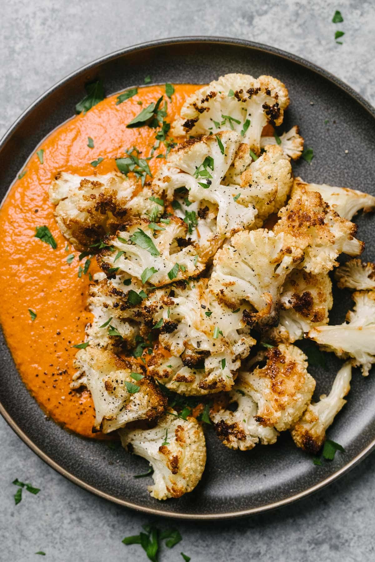 Roasted cauliflower florets with romesco sauce on a dark grey plate, garnished with fresh chopped parsley.