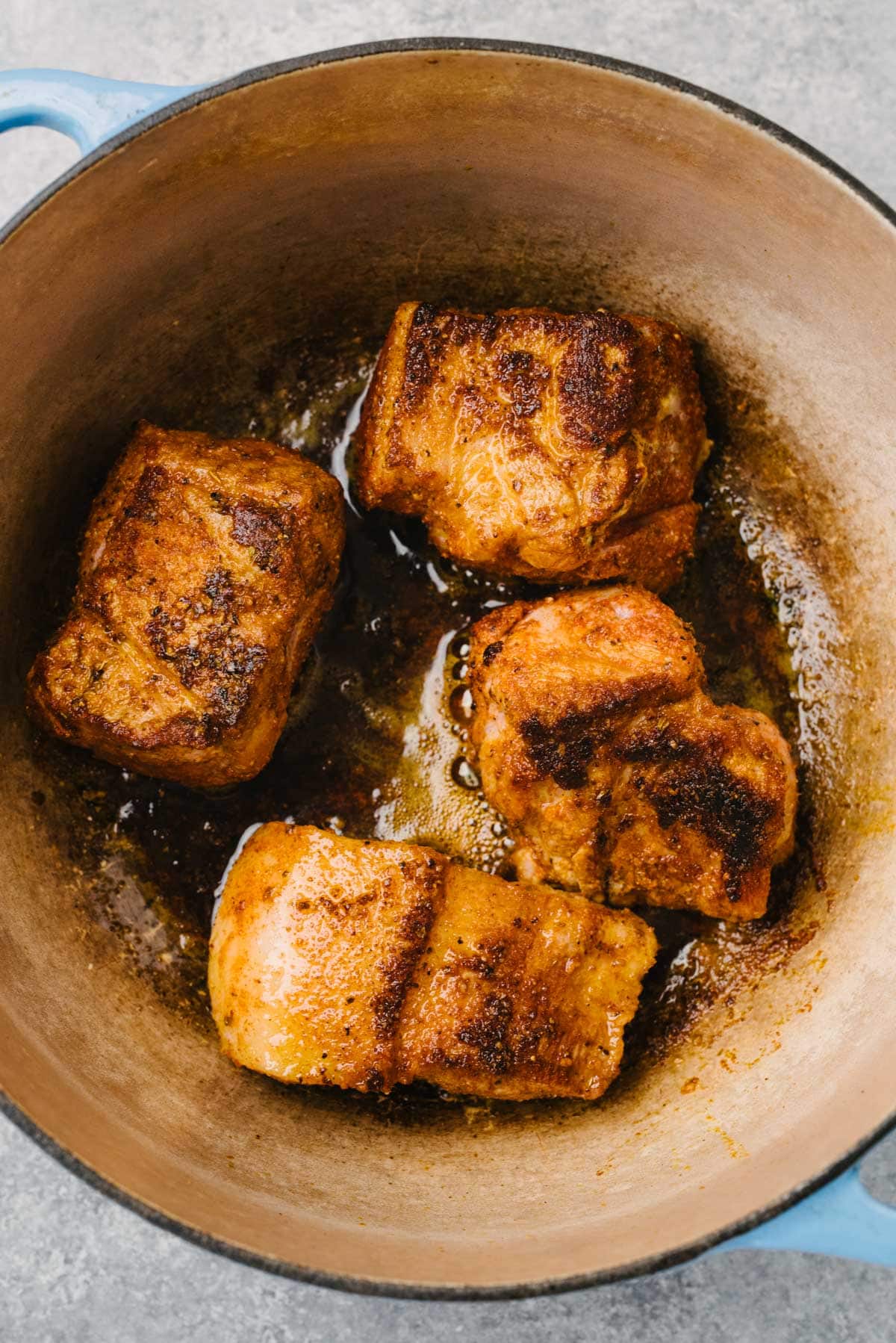 Seared pieces of boneless pork butt coated in dry rub being seared in a dutch oven.